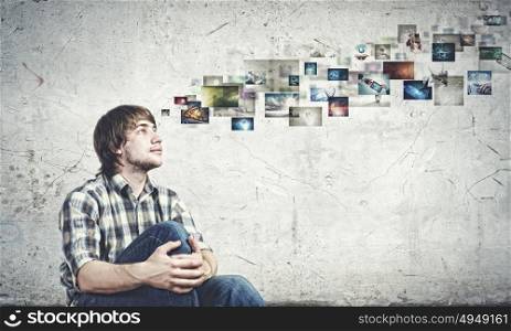 Photography concept. Young man in casual sitting on floor and looking at media photos