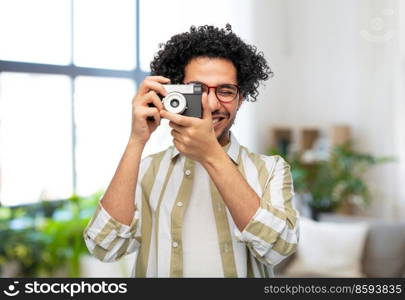 photography, hobby and people and concept - happy smiling man or photographer in glasses with film camera over home room background. smiling man or photographer with camera at home