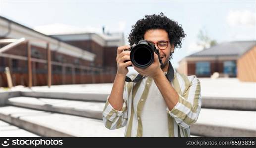 photography, profession and people and concept - happy smiling man or photographer in glasses with digital camera over city street background. smiling man or photographer with digital camera
