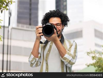 photography, profession and people and concept - happy smiling man or photographer in glasses with digital camera over city background. smiling man or photographer with digital camera