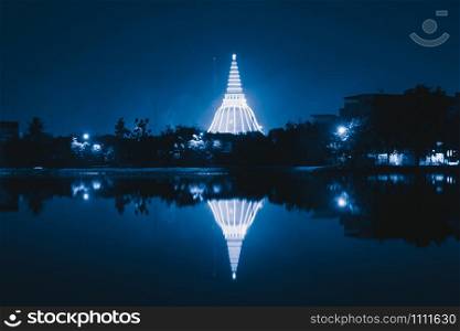 Phra Pathommachedi temple skyline with reflection at night. The golden buddhist pagoda with residential houses, urban city of Nakorn Pathom district, Thailand. Holy Thai architecture.