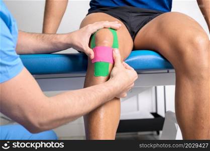 Physical therapist applying kinesio tape on male patient knee. Kinesiology, physical therapy, rehabilitation concept. close up. High quality photo. Physical therapist applying kinesio tape on male patient knee. Kinesiology, physical therapy, rehabilitation concept. close up