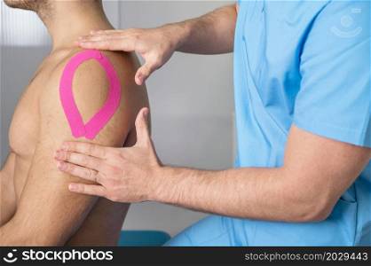 Physical therapist applying kinesio tape on male patient knee. Kinesiology, physical therapy, rehabilitation concept. close up. High quality photo. Physical therapist applying kinesio tape on male patient shoulder. Kinesiology, physical therapy, rehabilitation concept. close up