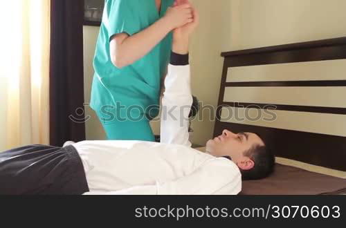 Physical therapist doing rehabilitation exercises for arms to young adult in bed.