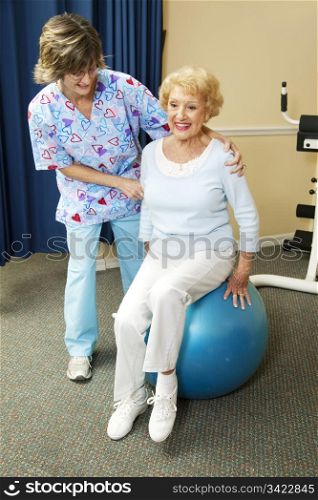Physical therapist helps a senior woman exercise on a pilates ball.