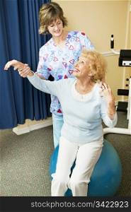 Physical therapist helps senior woman workout on a pilates ball.