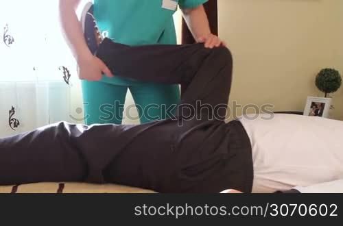 Physical therapist working rehabilitation exercises for legs with immobilized patient.