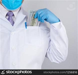 physician in a white coat, wearing blue sterile gloves, doctor holds a pack of paper money, anti-corruption concept, bribe and payment for the work done