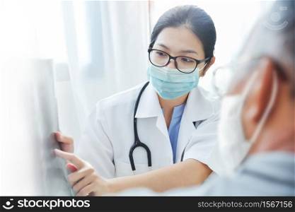 Physician talking with senior man at clinic pandemic during Covid-19 or Coronavirus. Asian woman Doctor wear eyeglasses and surgical mask giving advice to Elderly patient in medical room at hospital