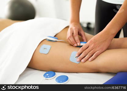 Physiotherapist applying electro stimulation in physical therapy to a young woman. Medical check at the leg in a physiotherapy center.