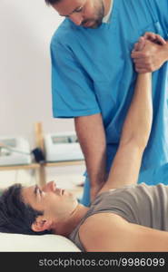 Physiotherapist doing healing treatment on man’s arm, Therapist wearing blue uniform, Osteopath,  Chiropractic adjustment, patient lying on massage table