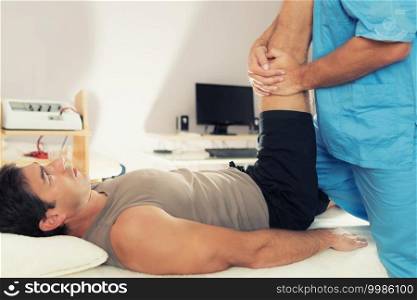 Physiotherapist doing healing treatment on patient leg. Therapist wearing blue uniform. Osteopathy. Chiropractic adjustment, patient lying on massage table