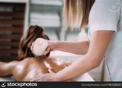 Physiotherapist drips wax from candle and massaging female patient’s back.. Candle Wax Massage