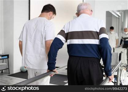 Physiotherapist helping senior patient walk between parallel bars. High quality photo. Physiotherapist helping senior patient walk between parallel bars.