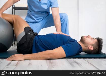Physiotherapist helps handsome young patient with pilates exercises. High quality photo. Physiotherapist helps handsome young patient with pilates exercises.