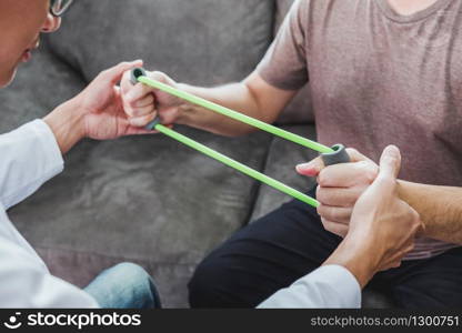 Physiotherapist man giving resistance band exercise treatment About Chest muscles and Shoulder of athlete male patient Physical therapy Visit the patient&rsquo;s home