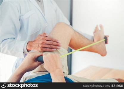Physiotherapist man giving resistance band exercise treatment About knee of athlete male patient Physical therapy concept