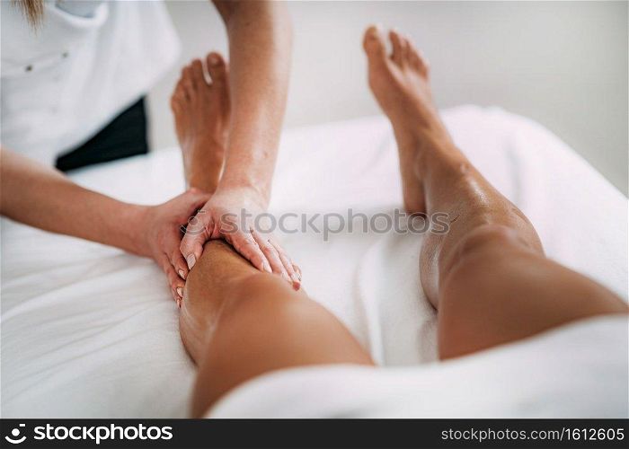 Physiotherapist massaging female patient with injured leg. Sports injury treatment.. Legs Sports Massage Therapy