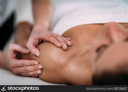 Physiotherapist massaging female patient with injured shoulder.  Sports injury treatment.. Shoulder Sports Massage Therapy