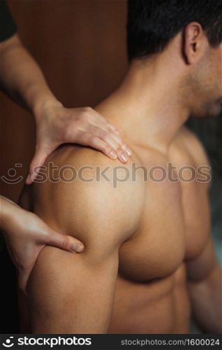 Physiotherapist massaging male patient with injured shoulder muscle. Sports injury treatment.