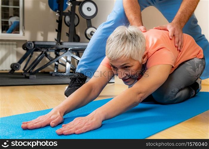 Physiotherapist or trainer stretching senior woman on exercise mat in the gym.. Physiotherapist Stretching Senior Woman