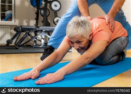 Physiotherapist or trainer stretching senior woman on exercise mat in the gym.. Physiotherapist Stretching Senior Woman