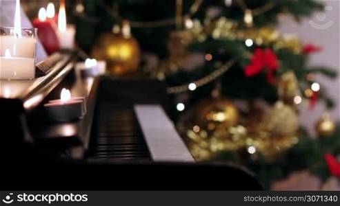 Piano keyboard with burning candles near Christmas tree.