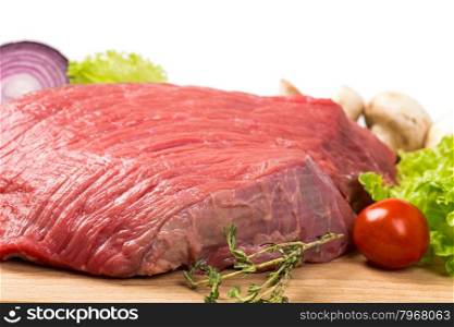 pice of fresh raw meat with lettuce, cherry, onion on wooden board