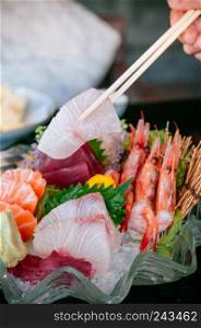 Picking Premiwith chopstick, Tai fish sashimi, Ebi sashimi, Maguro sashimi, salmon sashimi - Dark background warm tone image