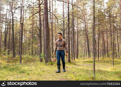 picking season and leisure people concept - happy smiling middle aged man with wicker basket of mushrooms walking in autumn forest. happy man with basket picking mushrooms in forest