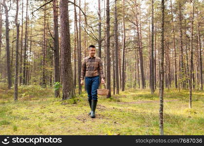 picking season and leisure people concept - happy smiling middle aged man with wicker basket of mushrooms walking in autumn forest. happy man with basket picking mushrooms in forest