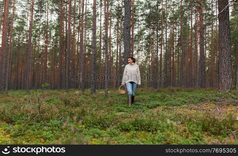 picking season and leisure people concept - young woman with mushrooms in wicker basket walking in forest. woman with basket picking mushrooms in forest