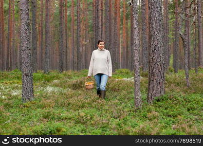 picking season and leisure people concept - young woman with mushrooms in wicker basket walking in forest. woman with basket picking mushrooms in forest