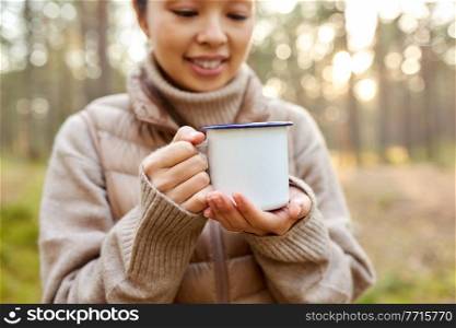 picking season, leisure and people concept - close up of young asian woman with mug drinking tea in autumn forest. asian woman with mug drinking tea in forest