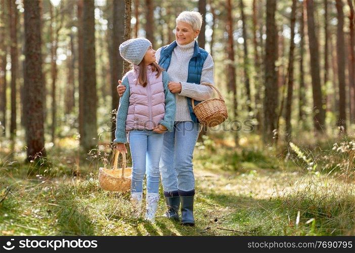 picking season, leisure and people concept - grandmother and granddaughter with baskets and mushrooms in forest. grandmother and granddaughter picking mushrooms