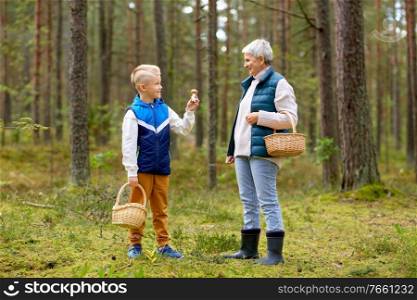 picking season, leisure and people concept - happy smiling grandmother and grandson with baskets and mushrooms in forest. grandmother and grandson with mushrooms in forest