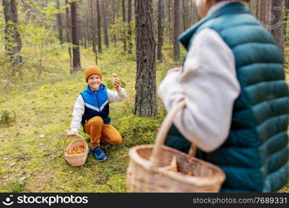 picking season, leisure and people concept - happy smiling grandmother and grandson with baskets and mushrooms in forest. grandmother and grandson with mushrooms in forest