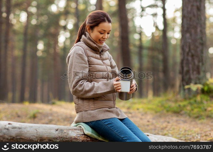 picking season, leisure and people concept - young asian woman with thermos and mug drinking tea in autumn forest. asian woman with thermos drinking tea in forest