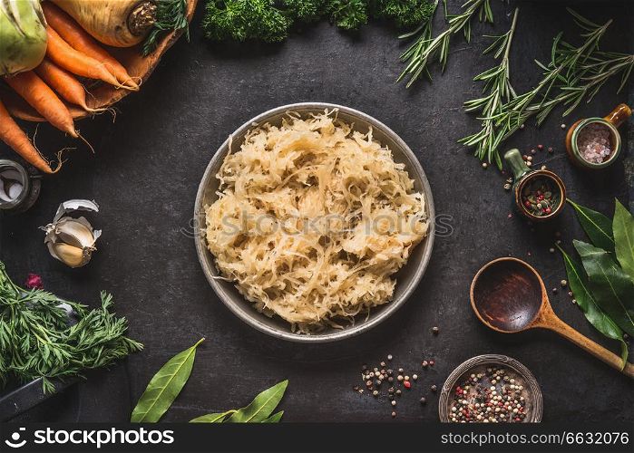 Pickled cabbage in bowl on dark rustic kitchen table background with cooking spoon and ingredients, top view. Healthy clean vegetarian low-calorie food concept