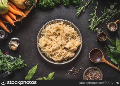 Pickled cabbage in bowl on dark rustic kitchen table background with cooking spoon and ingredients, top view. Healthy clean vegetarian low-calorie food concept
