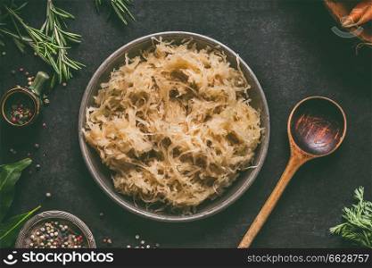 Pickled cabbage in bowl with wooden spoon and seasoning on dark rustic kitchen table background, top view. Vegetarian clean food. Paleo diet. Healthy eating concept