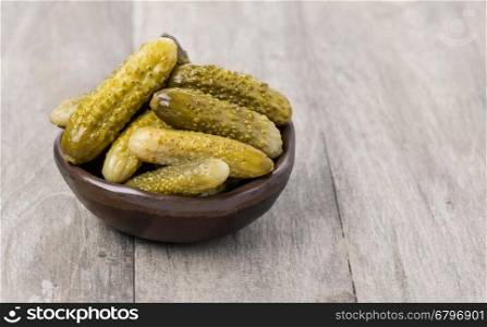 Pickled cucumbers in bowl on wooden background