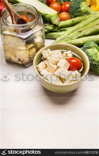 Pickled Diced feta cheese in olives oil and vegetables on white wooden background, border, close up
