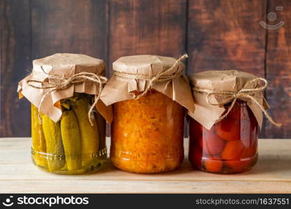 Pickled farm vegetables in glass jars on a wooden background. Fermented trending food. Home rustic style.. Pickled farm vegetables in glass jars on wooden background. Fermented trending food. Home rustic style.
