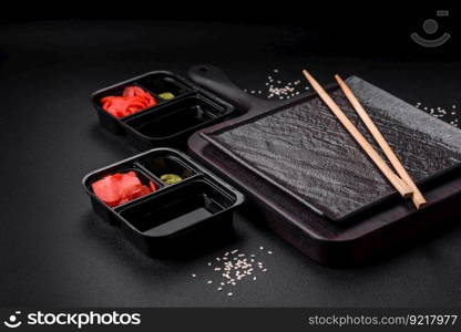 Pickled ginger, soy sauce and wasabi in portioned plastic containers on a dark concrete background