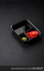 Pickled ginger, soy sauce and wasabi in portioned plastic containers on a dark concrete background