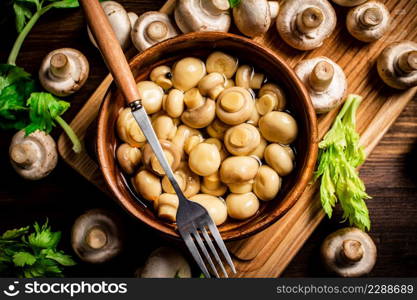 Pickled mushrooms in a bowl on a cutting board with greens. On a wooden background. High quality photo. Pickled mushrooms in a bowl on a cutting board with greens.