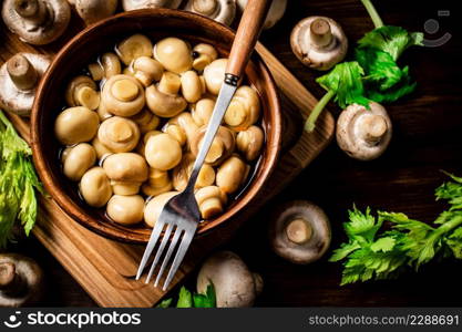 Pickled mushrooms in a bowl on a cutting board with greens. On a wooden background. High quality photo. Pickled mushrooms in a bowl on a cutting board with greens.