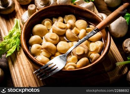 Pickled mushrooms in a bowl on a cutting board with greens. On a wooden background. High quality photo. Pickled mushrooms in a bowl on a cutting board with greens.