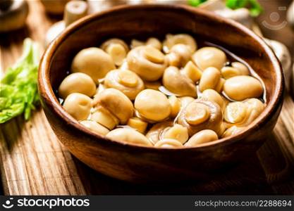 Pickled mushrooms in a bowl on a cutting board with greens. On a wooden background. High quality photo. Pickled mushrooms in a bowl on a cutting board with greens.
